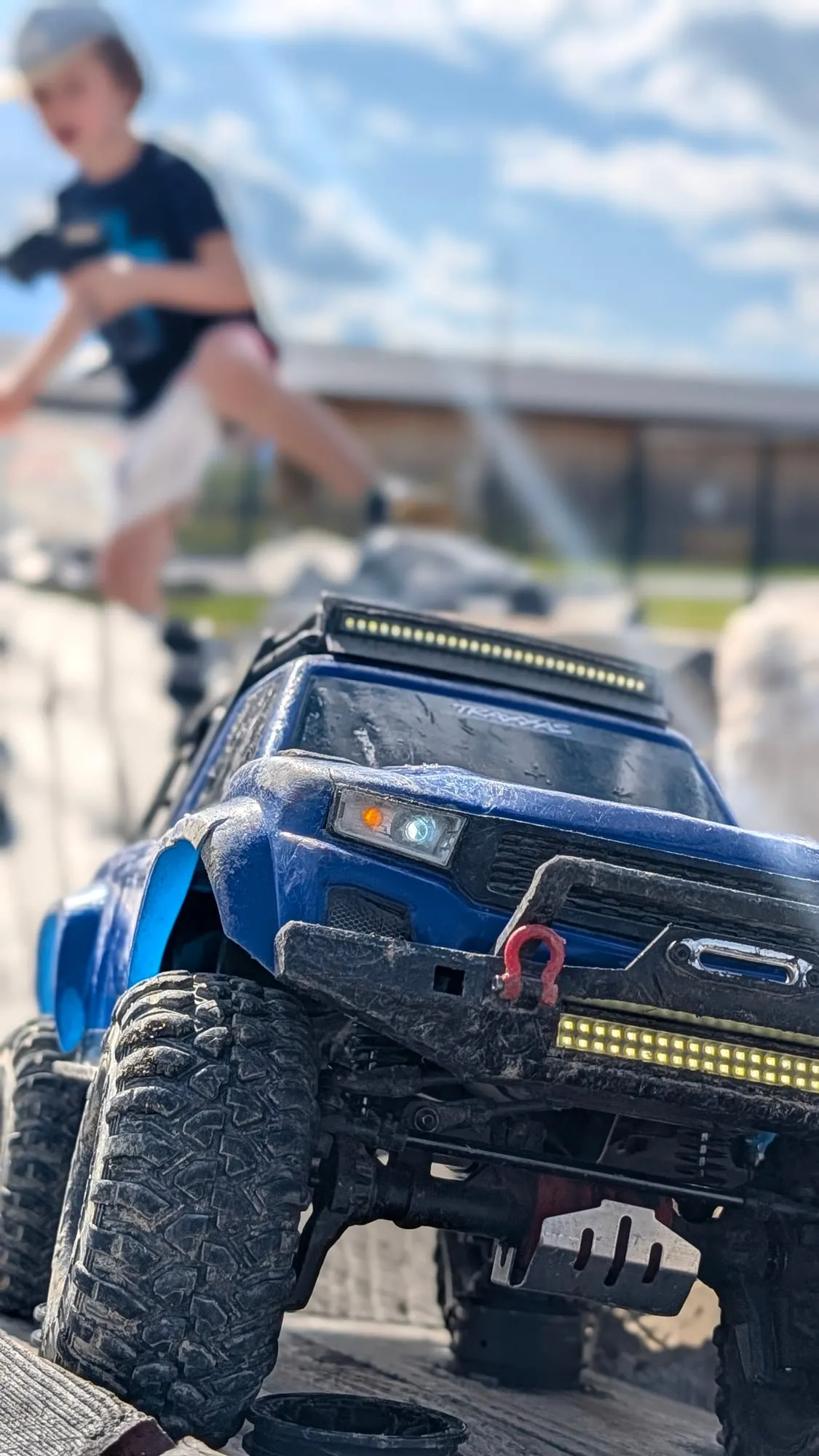 Nahaufnahme eines blauen RC-Trucks mit LED-Leuchtbalken beim Klettern über Steine