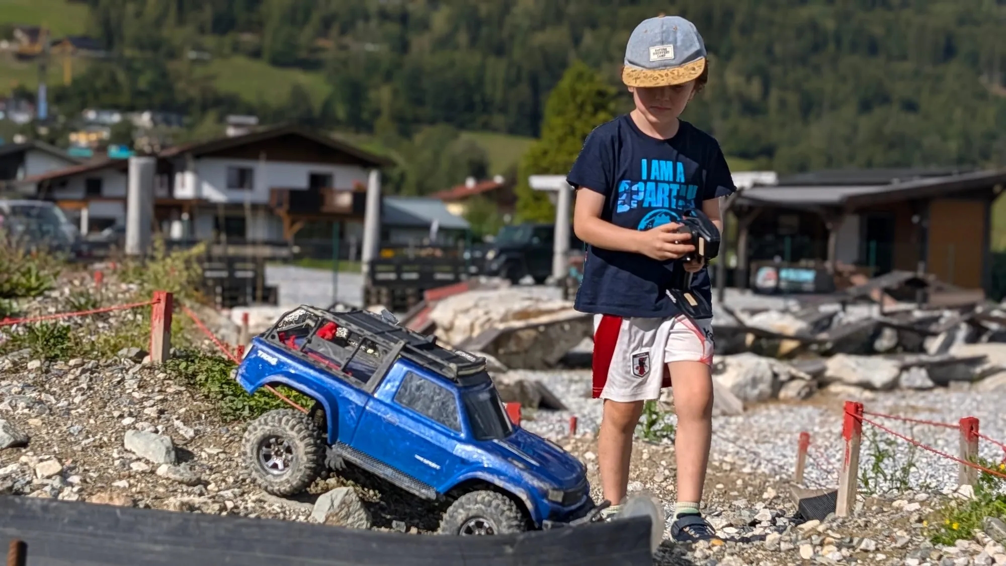 Mio lenkt einen blauen RC-Crawler über eine steinige Piste in den Bergen