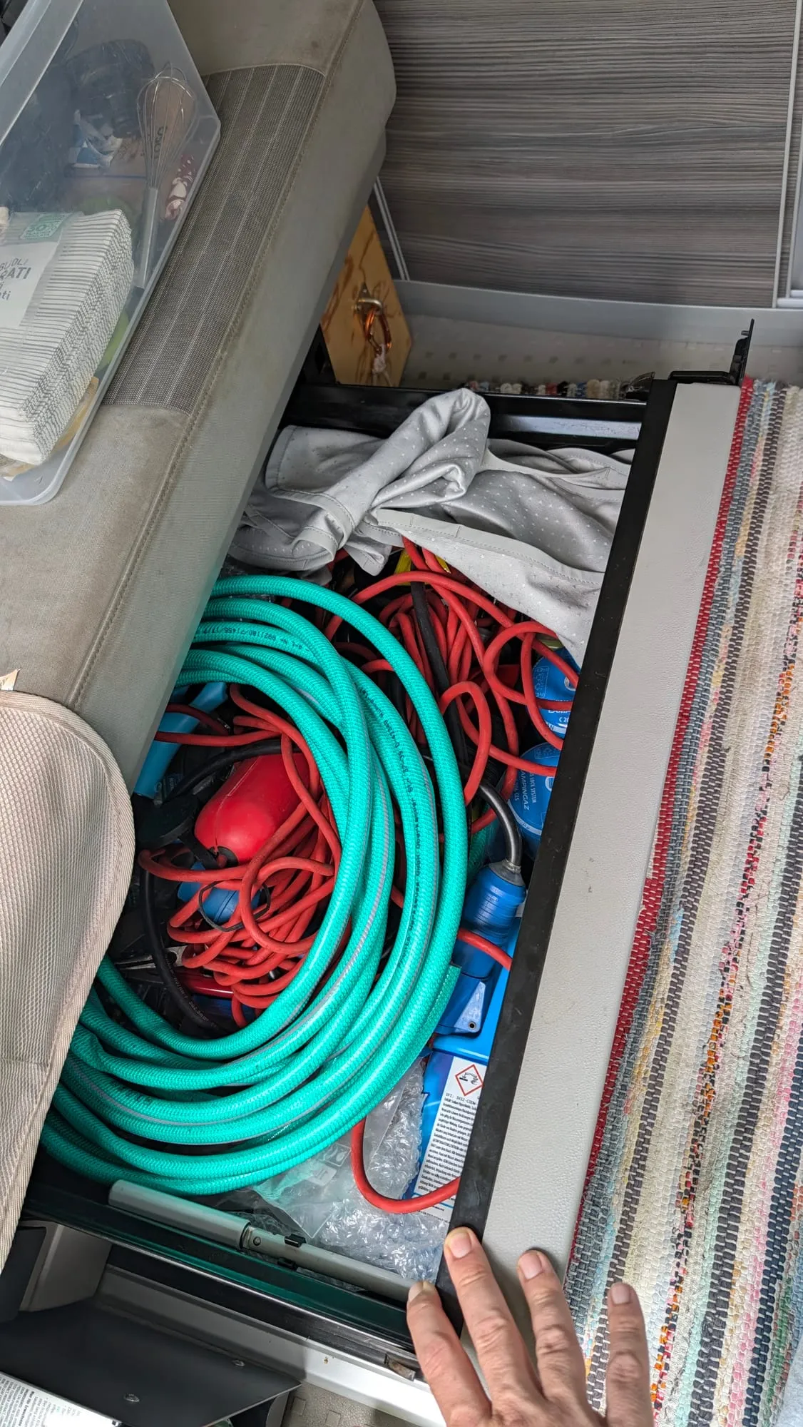Die ausgezogene Box unter der Hinterbank mit grünen und roten Schläuchen, Adaptern und Werkzeug
