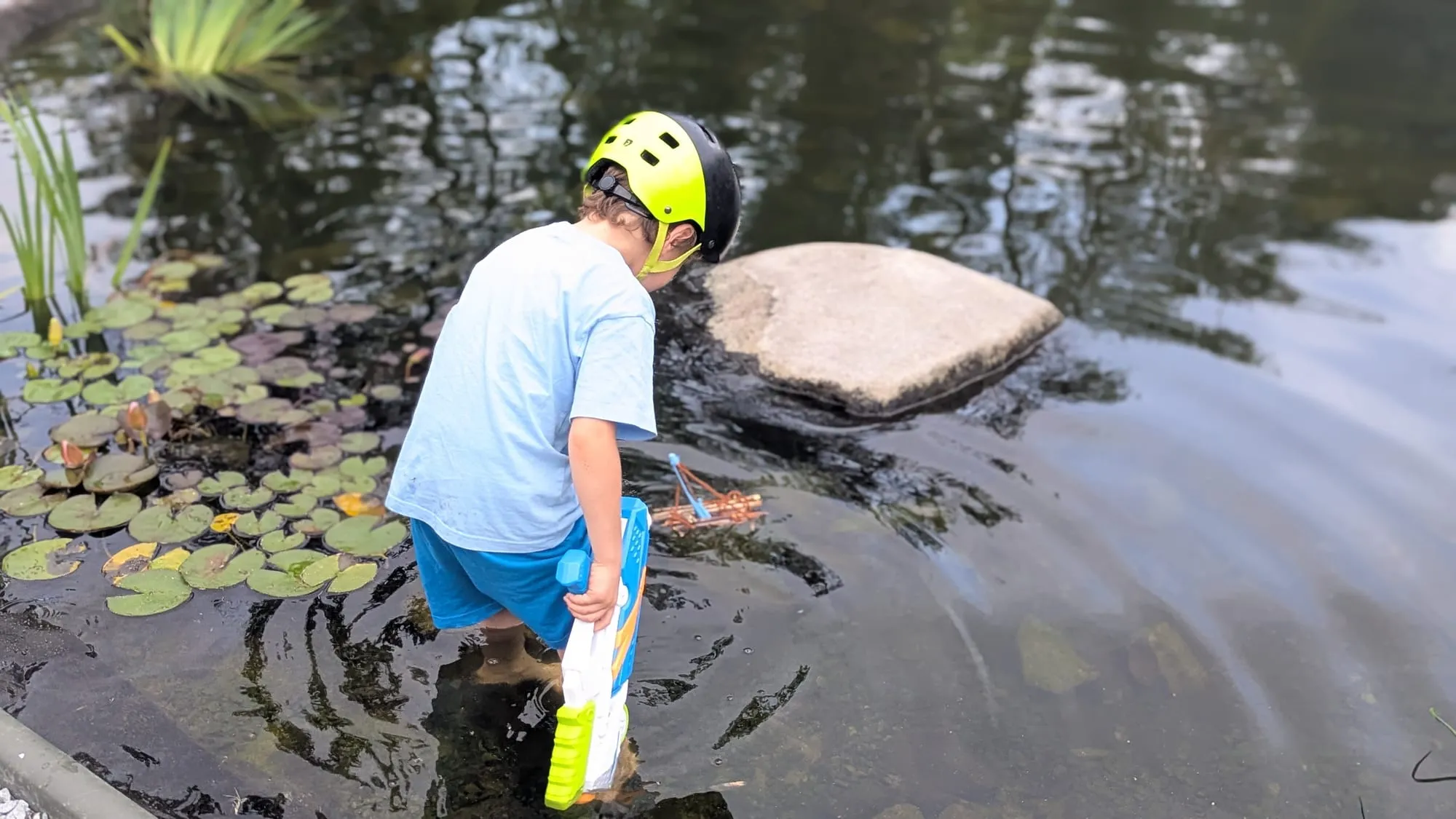 Mio steht mit Helm im Teich und schiebt das Floß mit der Hand an