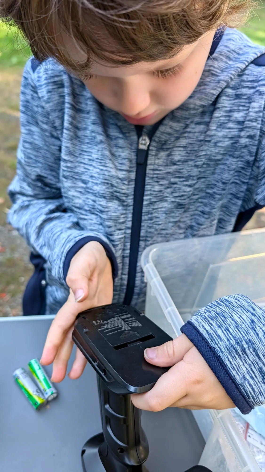 Mio wechselt die Batterien in der Fernsteuerung, während Papa die Hände hält