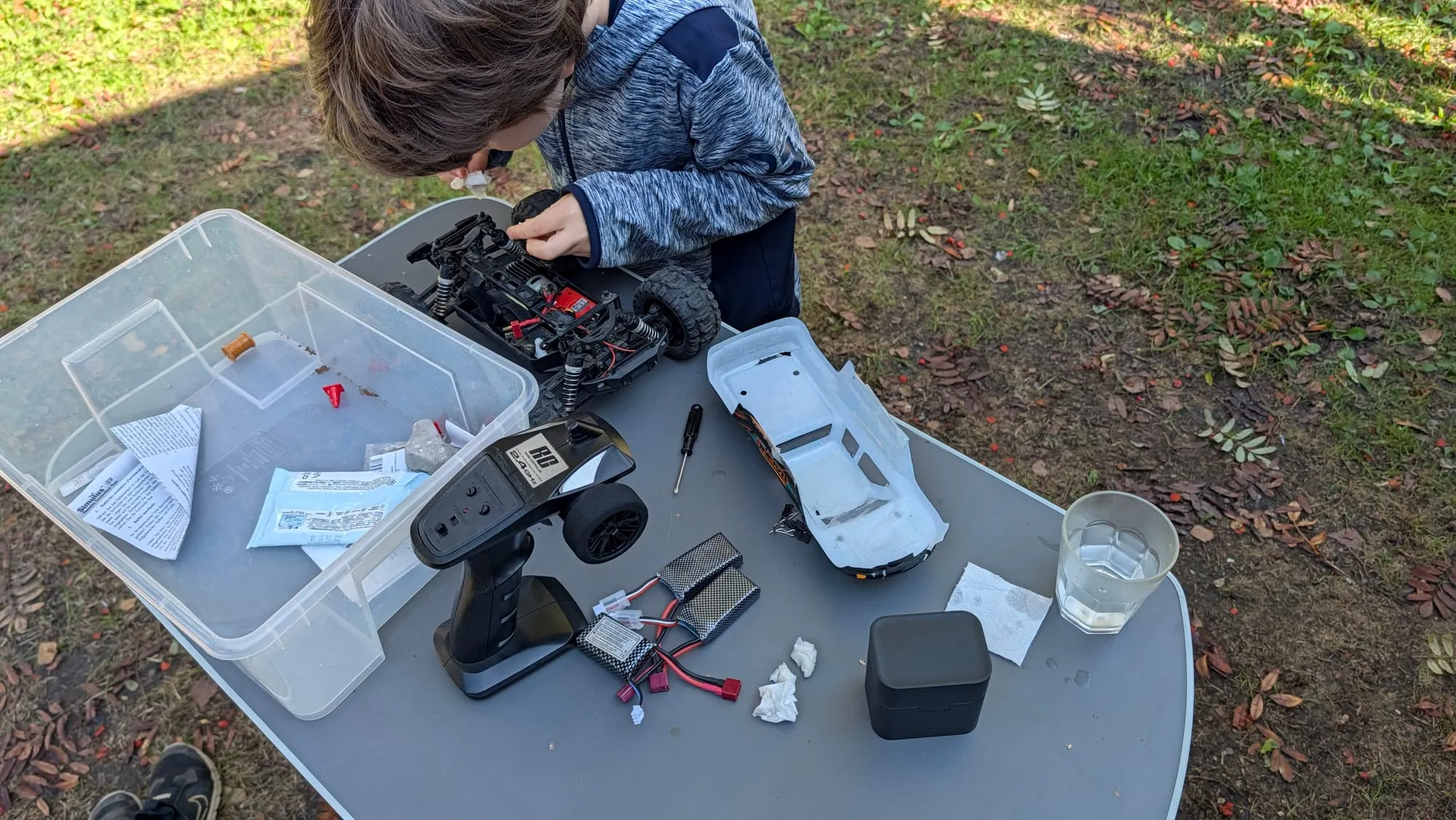 Zweites RC-Auto mit hellgrauer Karosserie neben Fernsteuerung und Akku auf dem Tisch